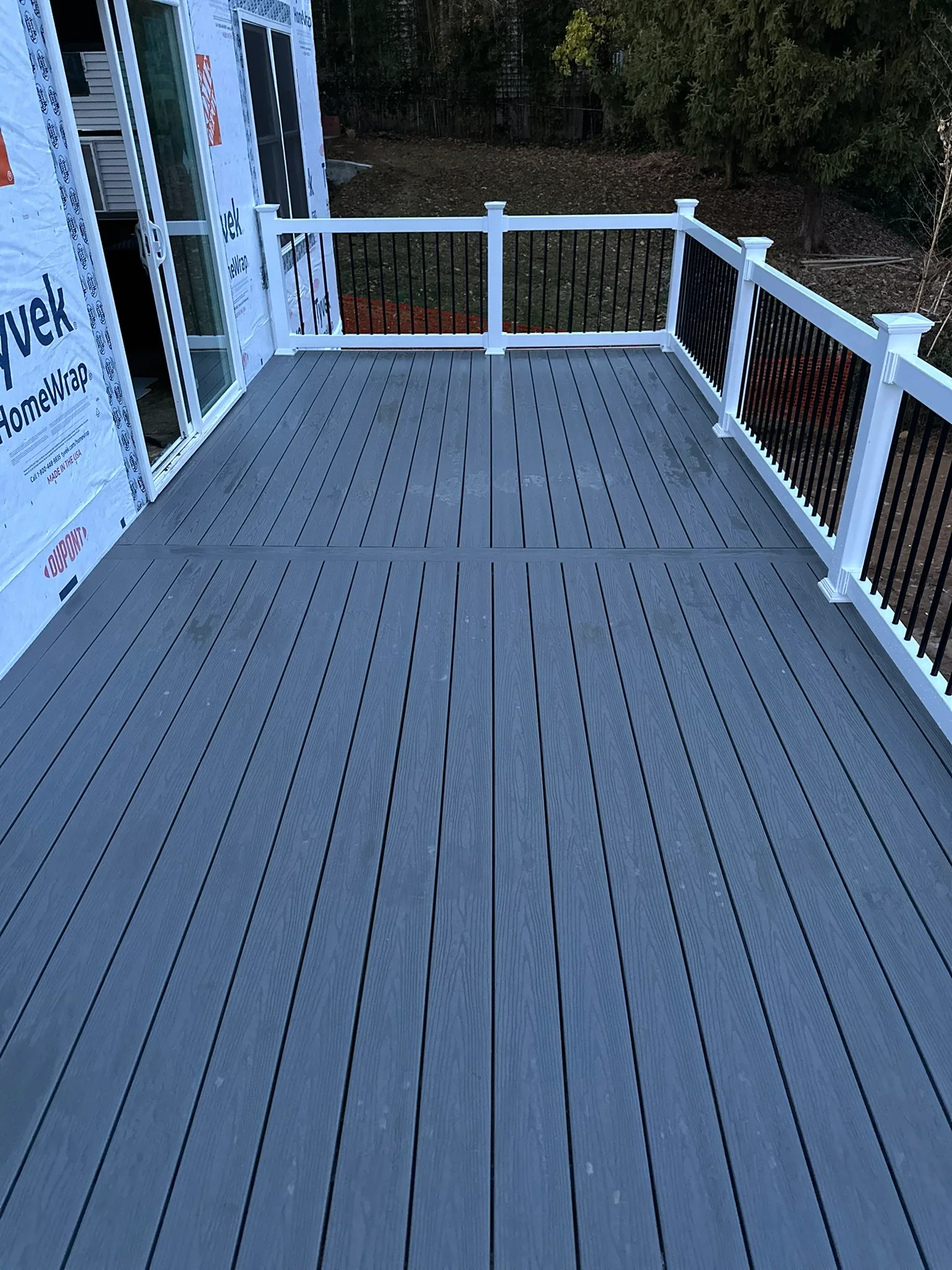Gray composite deck with white posts and black railing overlooking wooded yard