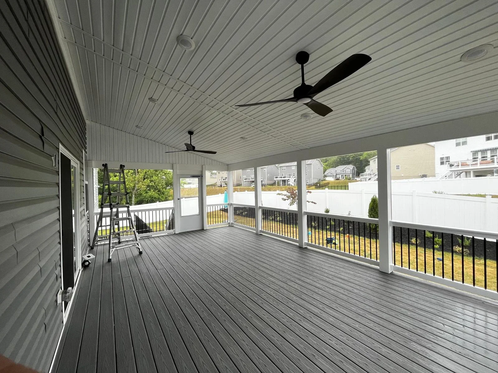 Large composite deck with metal roof patio, black railings, and ceiling fans overlooking backyard