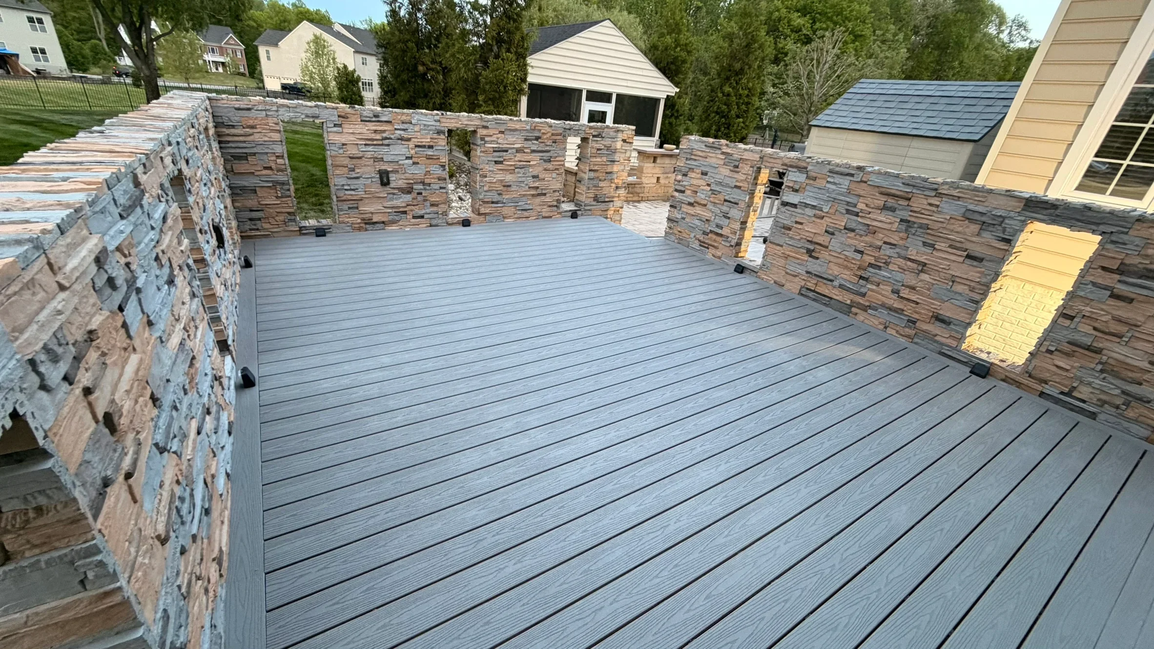 Gray composite deck with stacked stone veneer walls in residential backyard