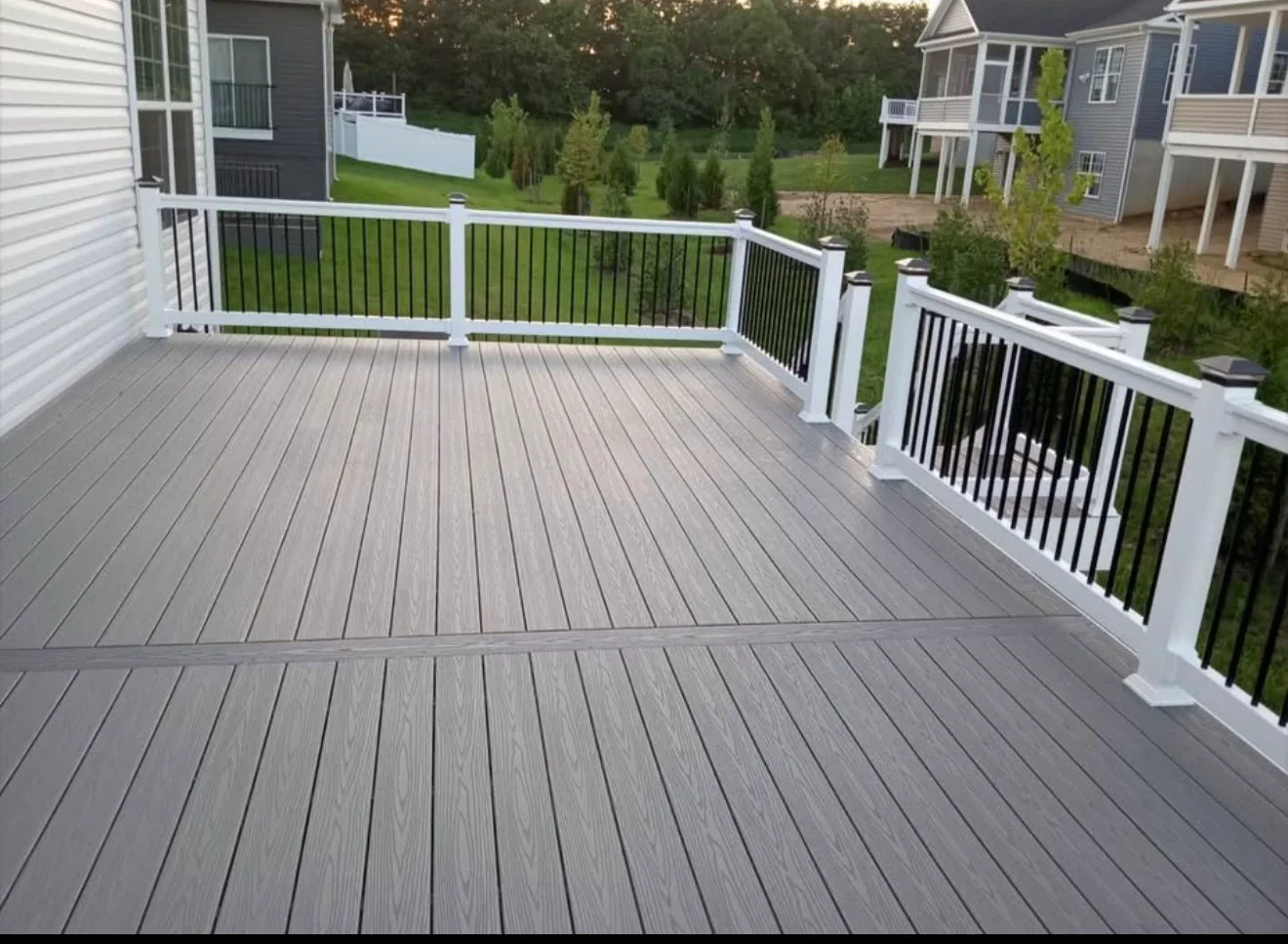 Large gray composite deck with white posts and black metal railing overlooking residential neighborhood