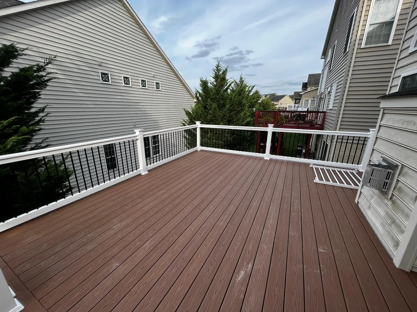 Brown composite deck with white vinyl railings and black metal balusters overlooking residential neighborhood
