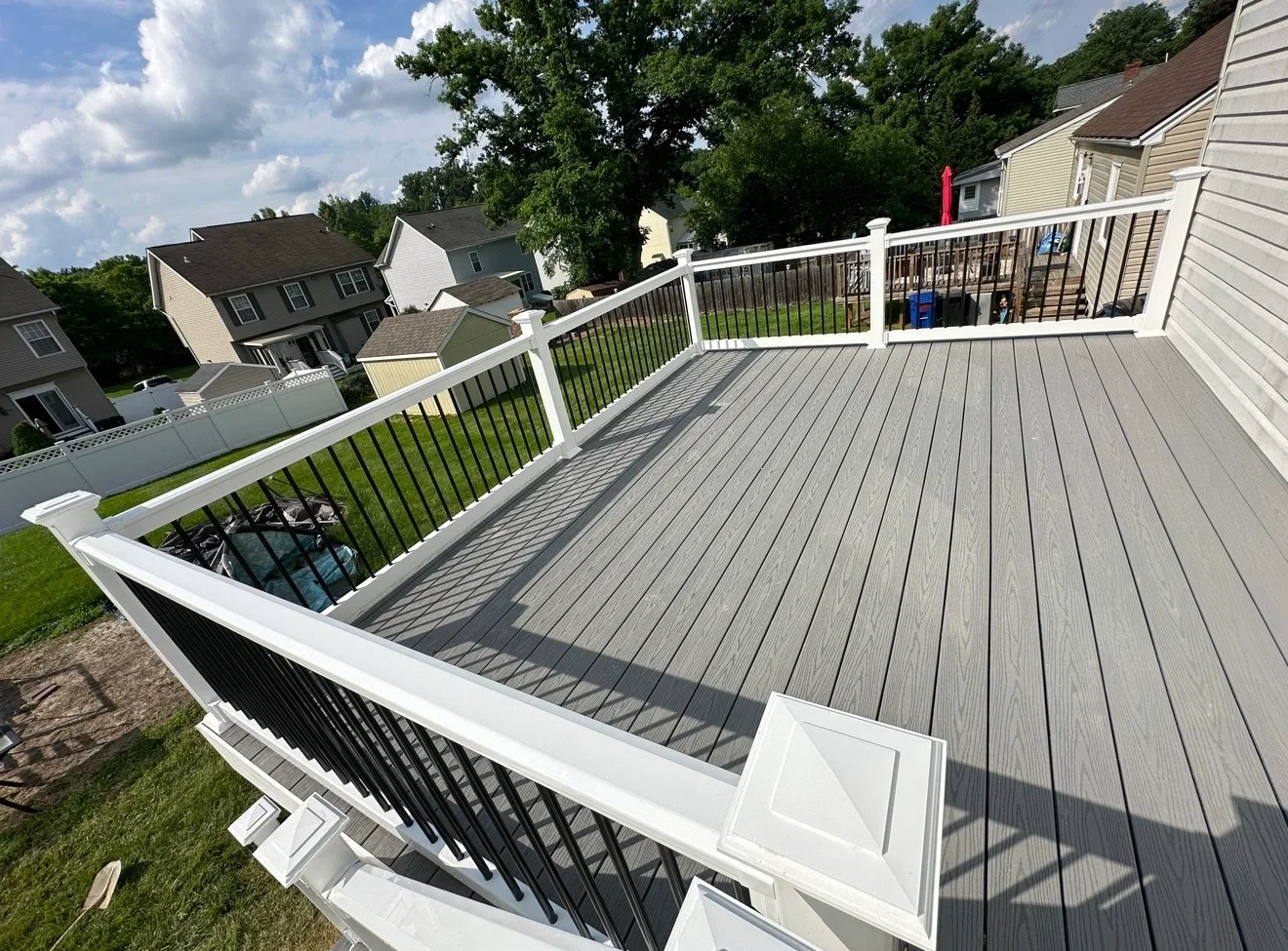 Two-level composite deck with white railings and black balusters overlooking residential neighborhood