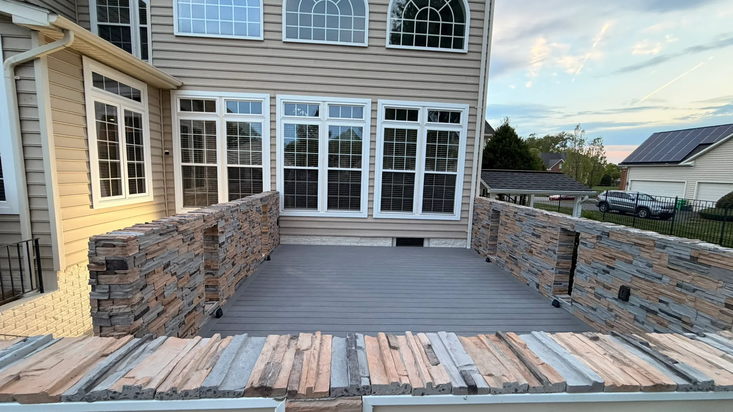 Gray composite deck with stone pillars and white-trimmed glass doors