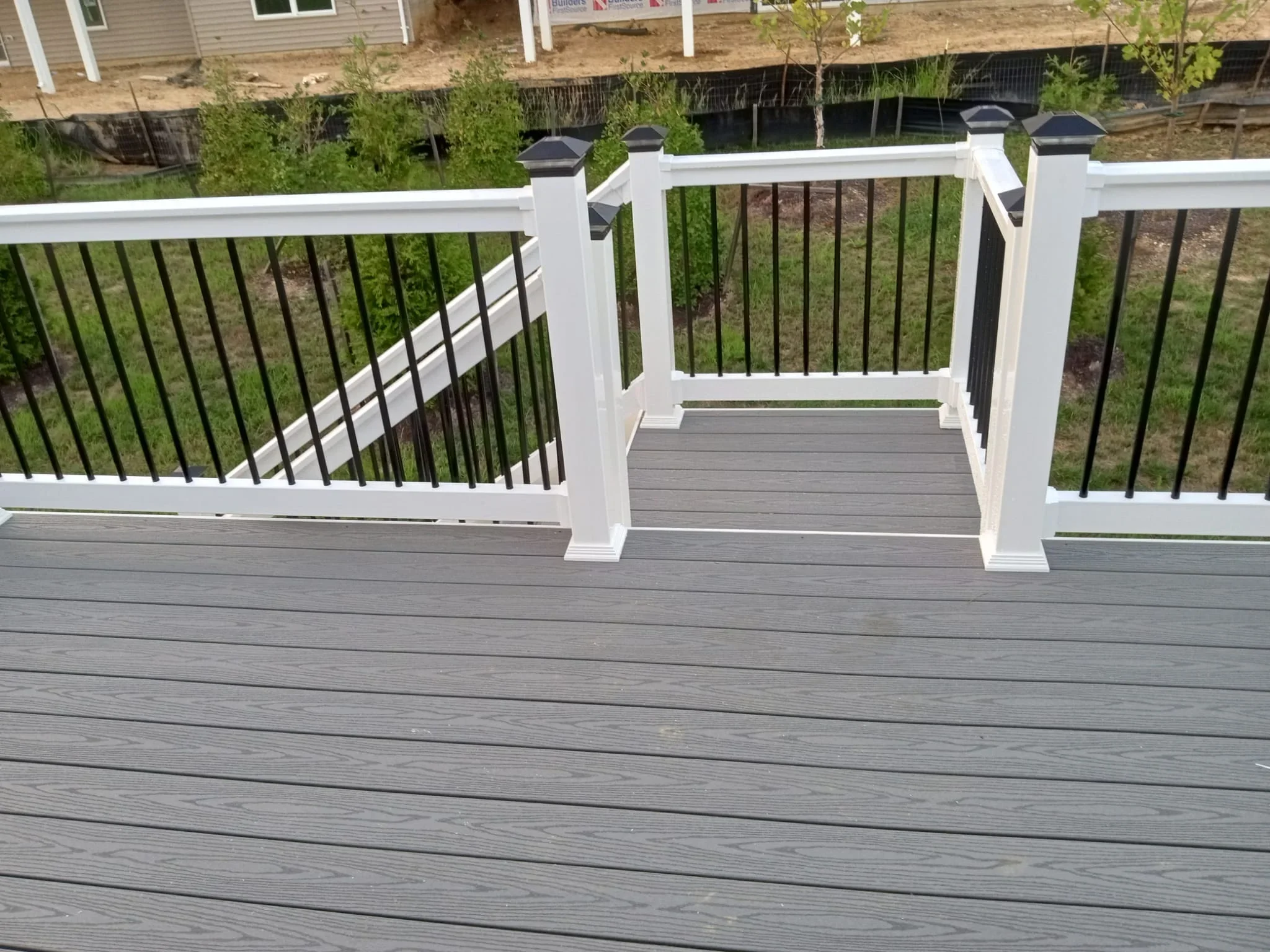 Gray composite deck with white railing and black balusters overlooking landscaped yard