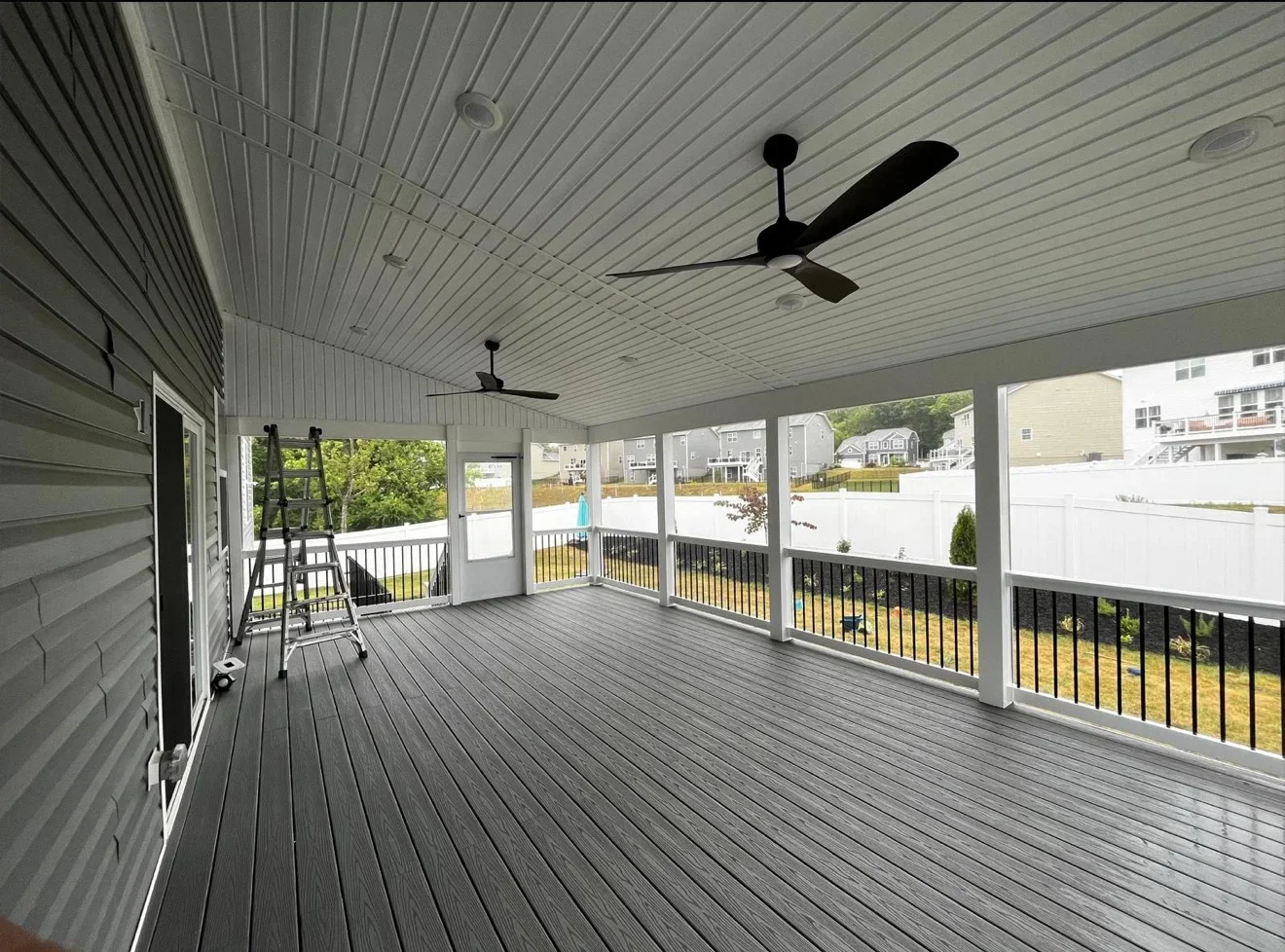 Large covered deck with gray composite flooring, metal roof, ceiling fans, and black metal railings