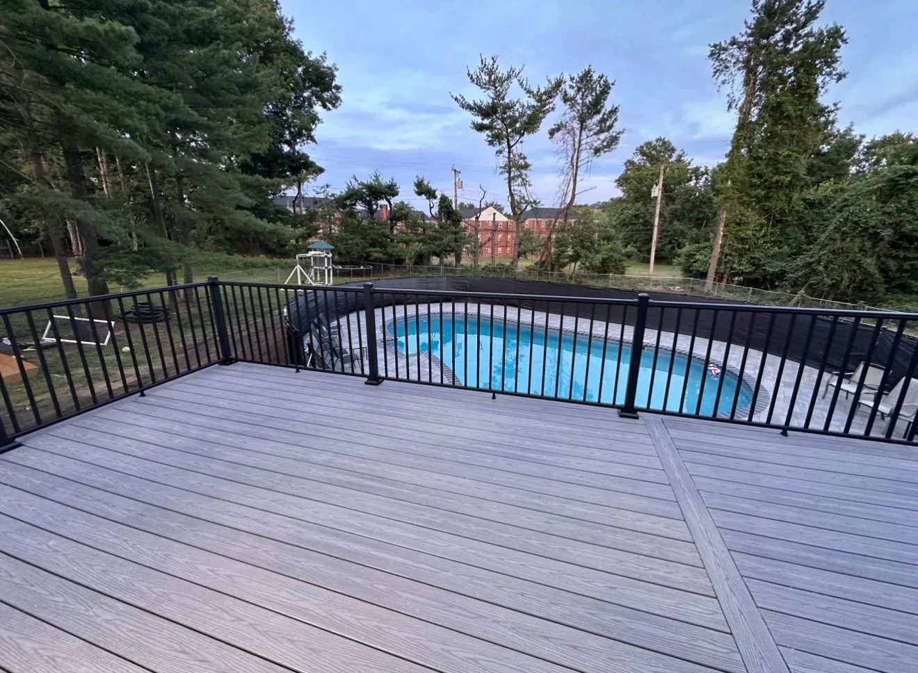 Gray composite deck with black metal railing overlooking backyard pool and trees