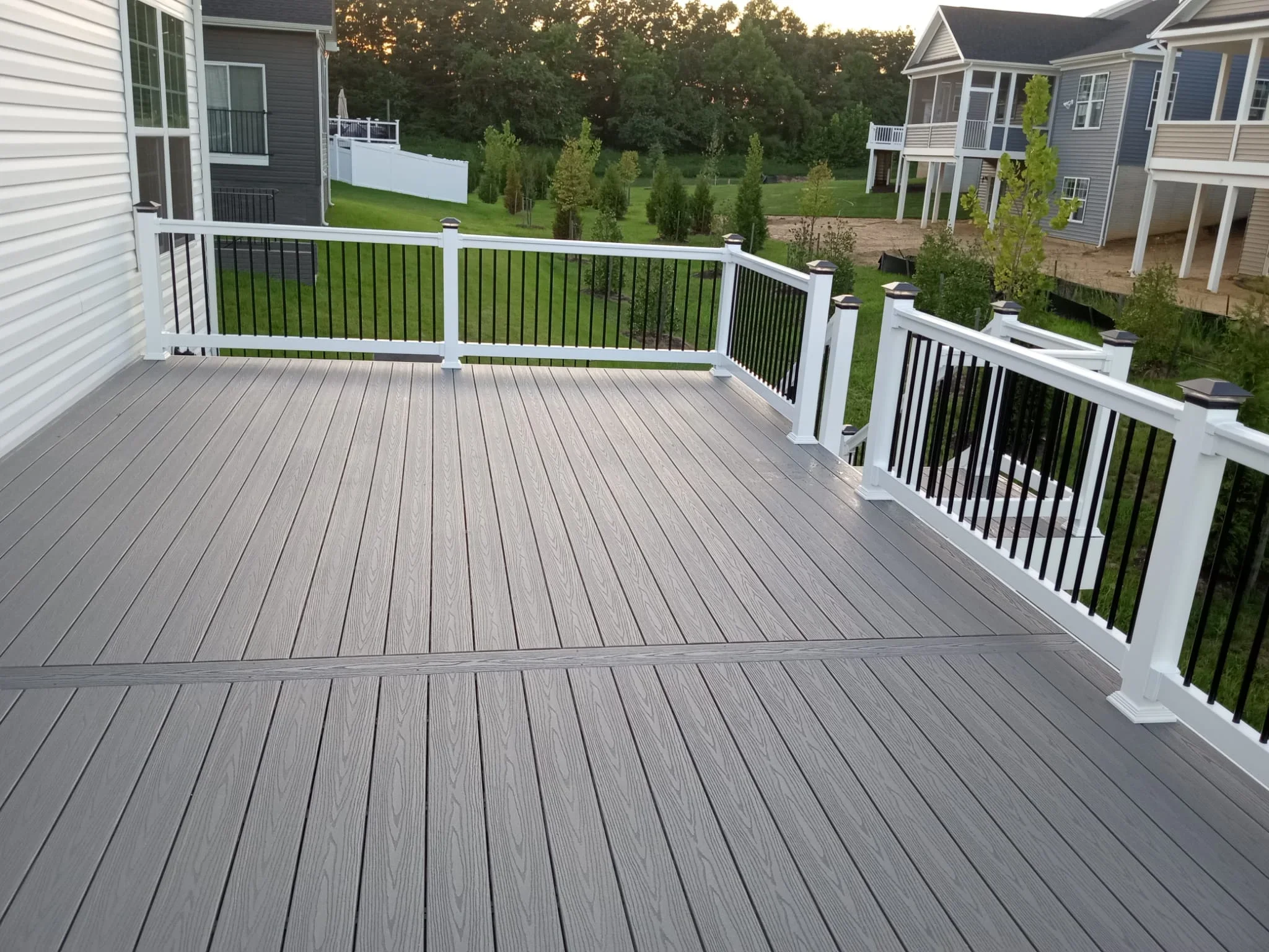 Gray composite deck with white vinyl railings and black balusters overlooking wooded residential neighborhood