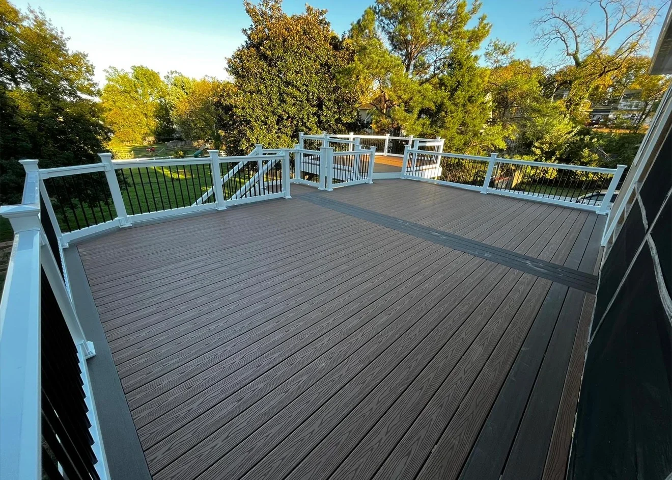 Large composite deck with white railings and black metal balusters overlooking wooded area