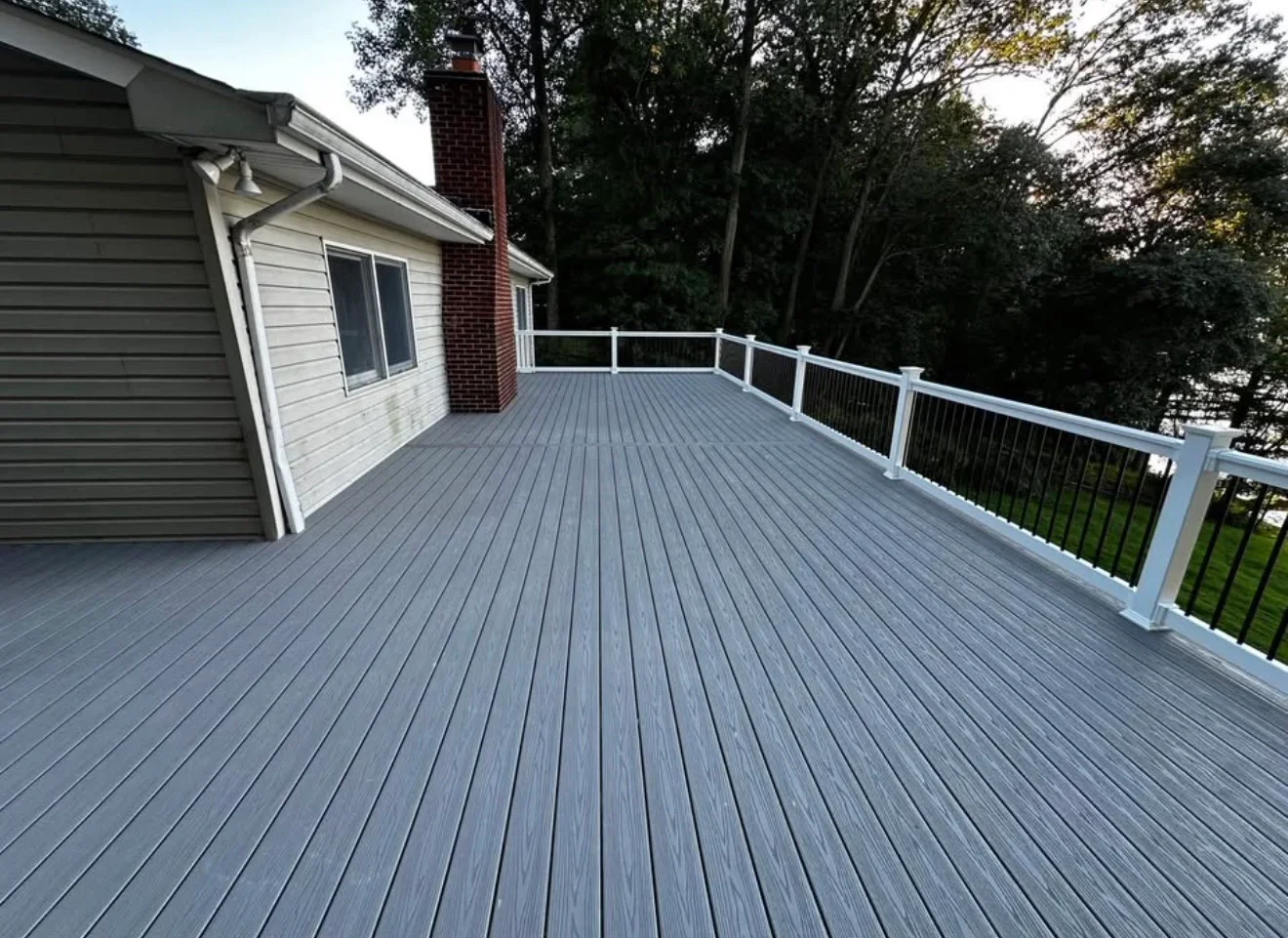 Large gray composite deck with white railing overlooking wooded area
