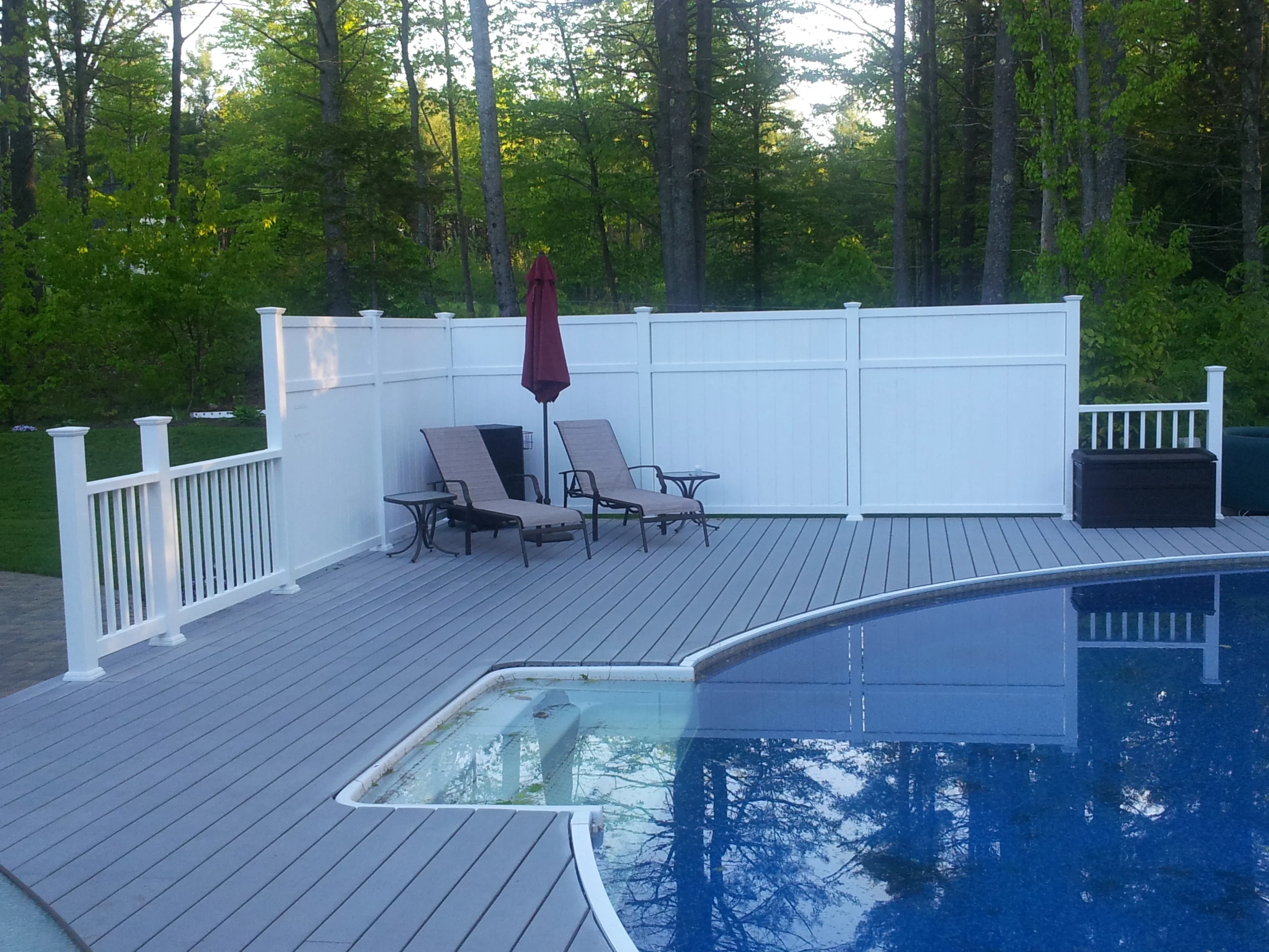 Gray composite deck with white privacy screen and railings surrounding pool area