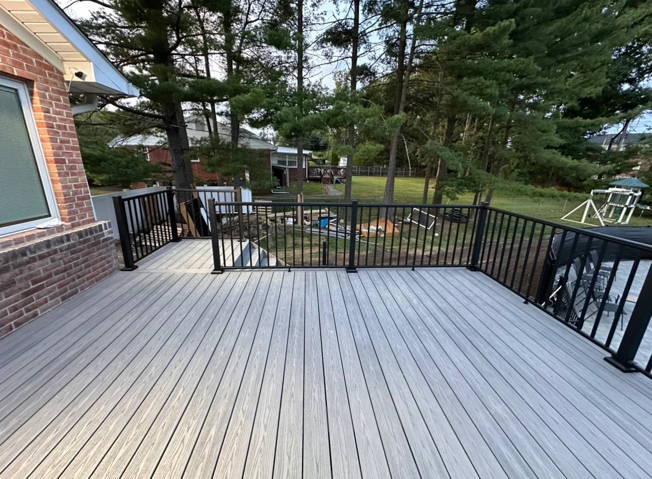 Large gray composite deck with black aluminum railings attached to brick home