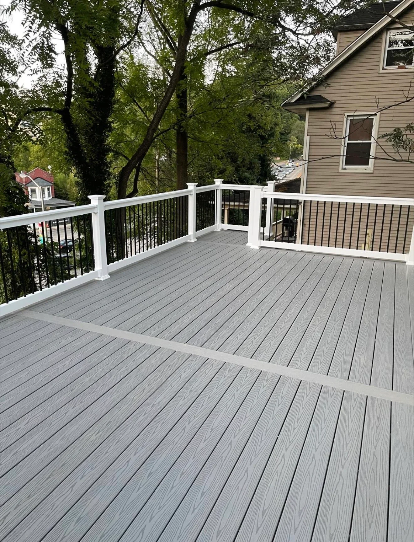 Gray composite deck with white vinyl railings and black metal balusters overlooking wooded area