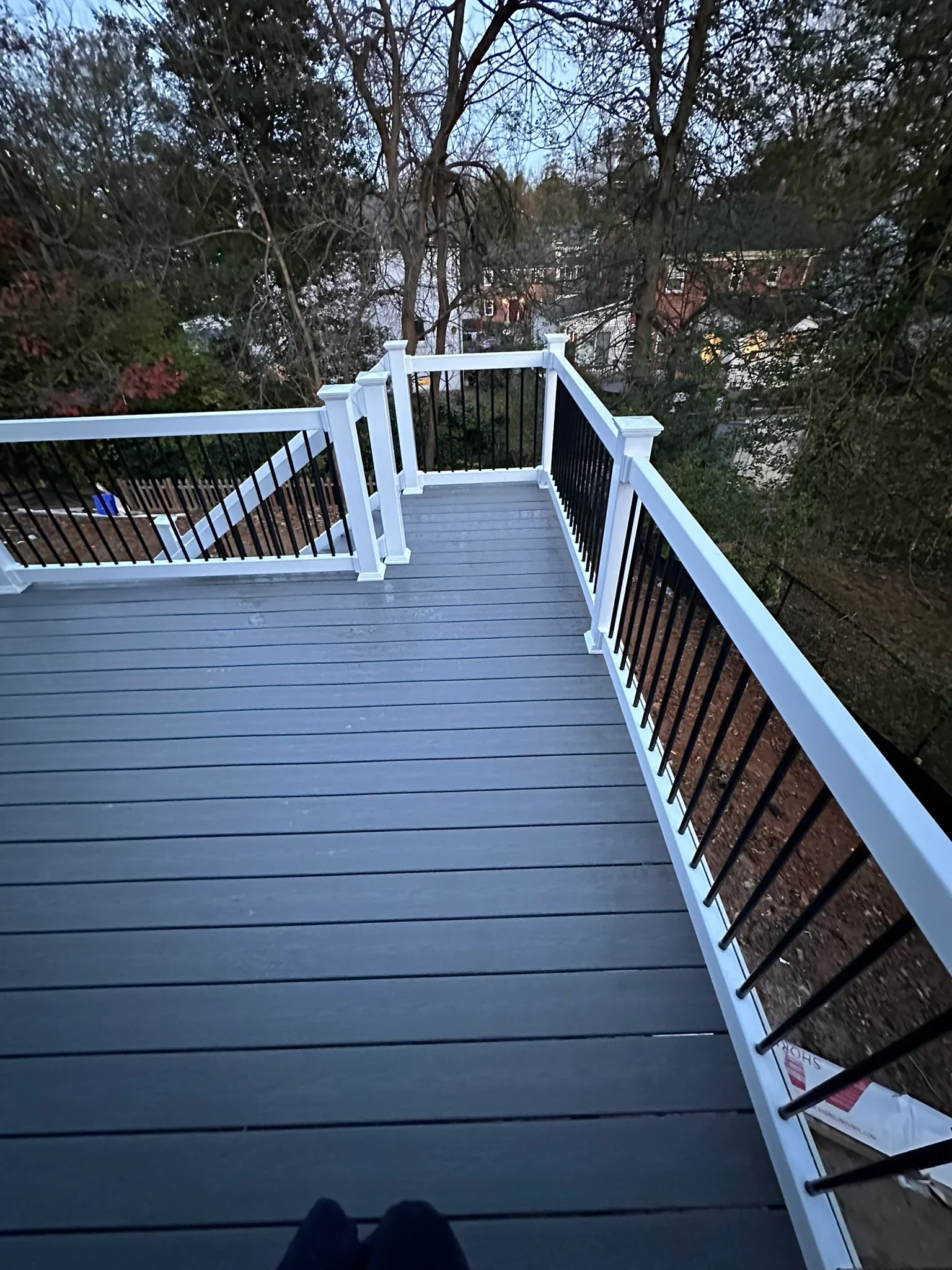 Multi-level gray composite deck with white railings and black metal balusters overlooking wooded area