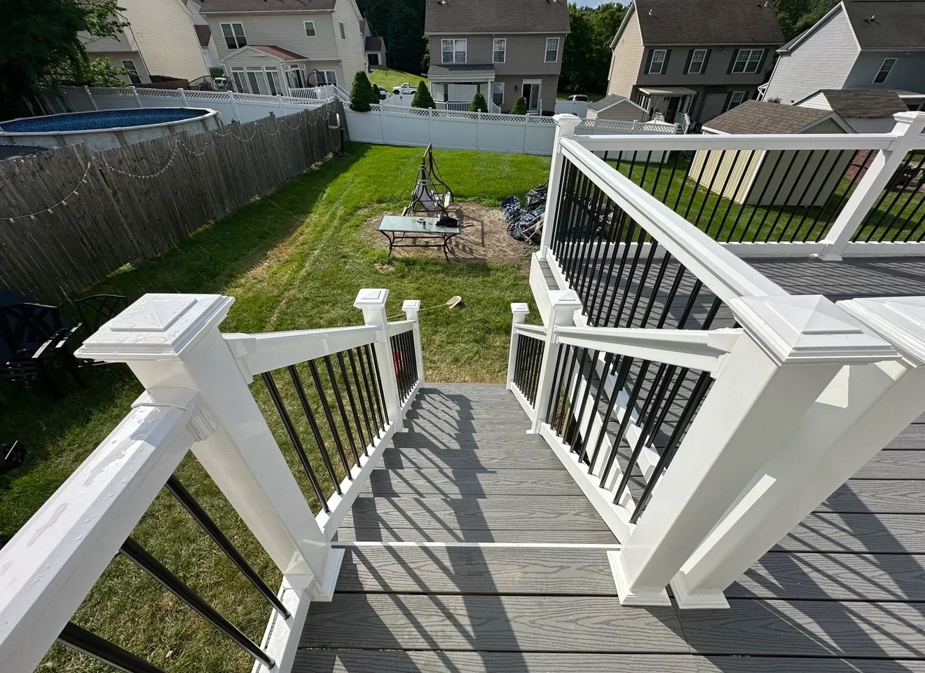 Multi-level gray composite deck with white trim and black railings overlooking backyard