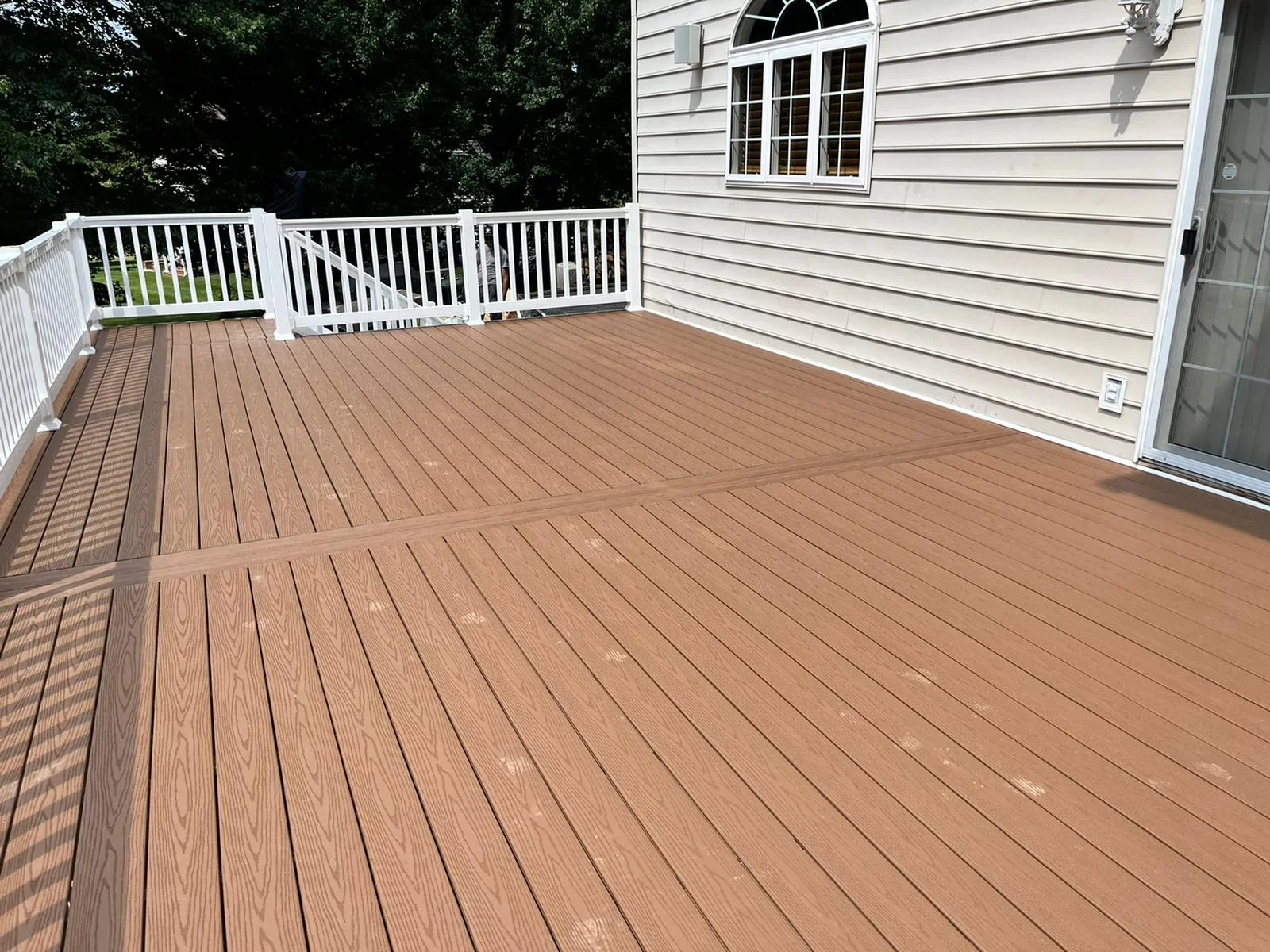 Large composite deck with brown boards and white vinyl railing attached to white-sided home