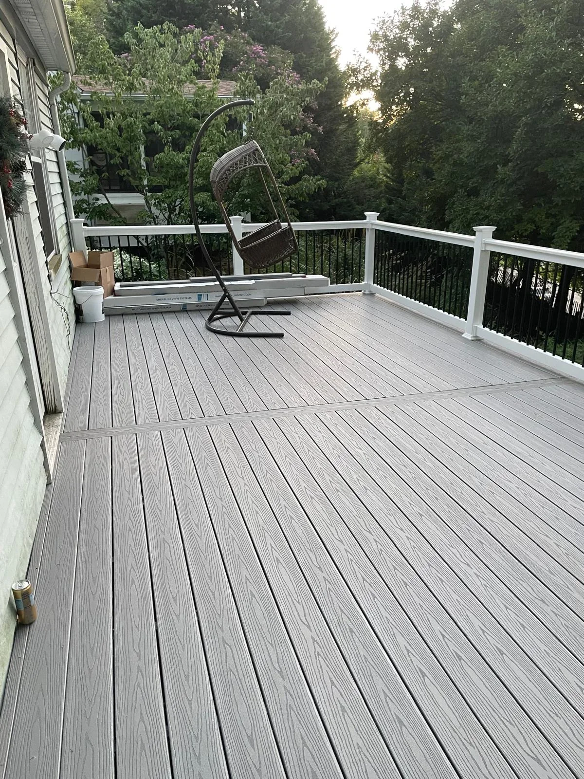 Gray composite deck with white vinyl railing and black balusters overlooking wooded landscape