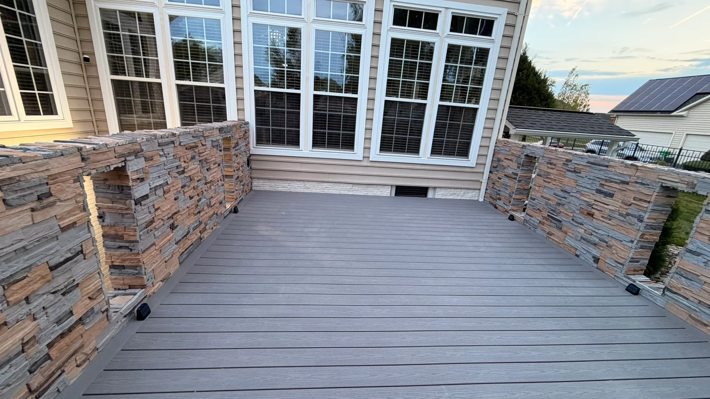 Gray composite deck with stone planter walls and large multi-pane windows overlooking landscape