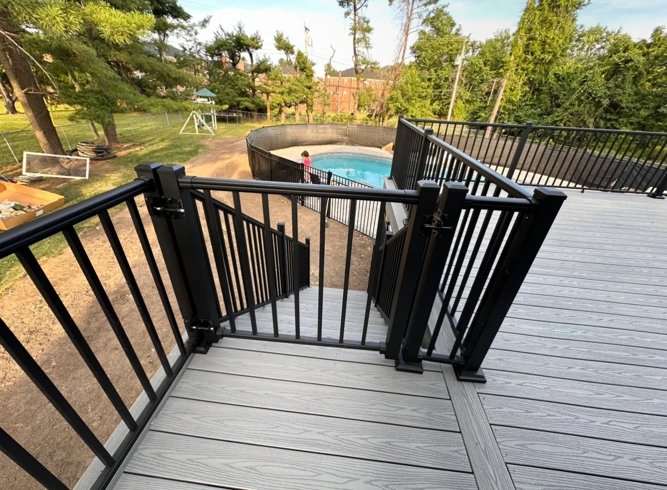 Gray composite deck with black aluminum railings overlooking in-ground pool and backyard