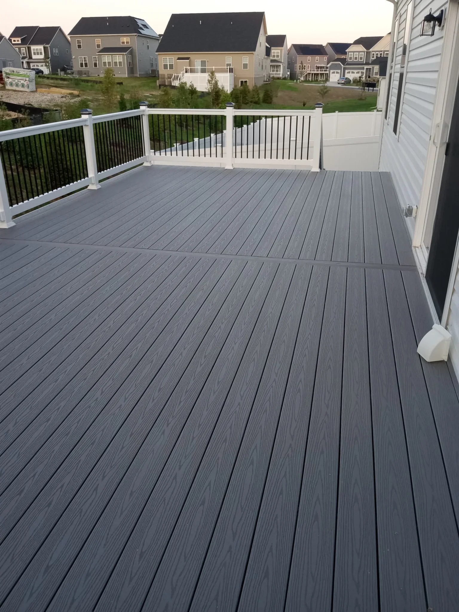 Gray composite deck with white posts and black metal railings overlooking residential neighborhood